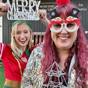 Image of two women in Chtristmassy clothes holding a merry christmas sign